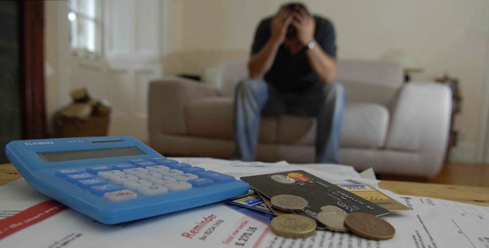 man holds head in hands, credit cards bills money for debt